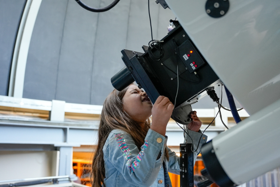 Young girl looking through the eye piece of a telescope