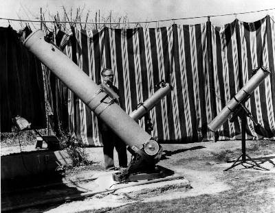 Norman standing behind his teliscope in his makeshift curtain observatory